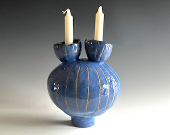 May include: A blue ceramic candle holder with two candle cups and a striped design. The candle holder is shaped like a sphere with a small base.