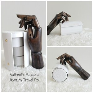 May include: White travel roll for jewelry with three compartments. The roll is made of faux leather and has a white embossed pattern. The roll is closed with a zipper. The text "Authentic Pandora Jewelry Travel Roll" is printed on the bottom of the image.