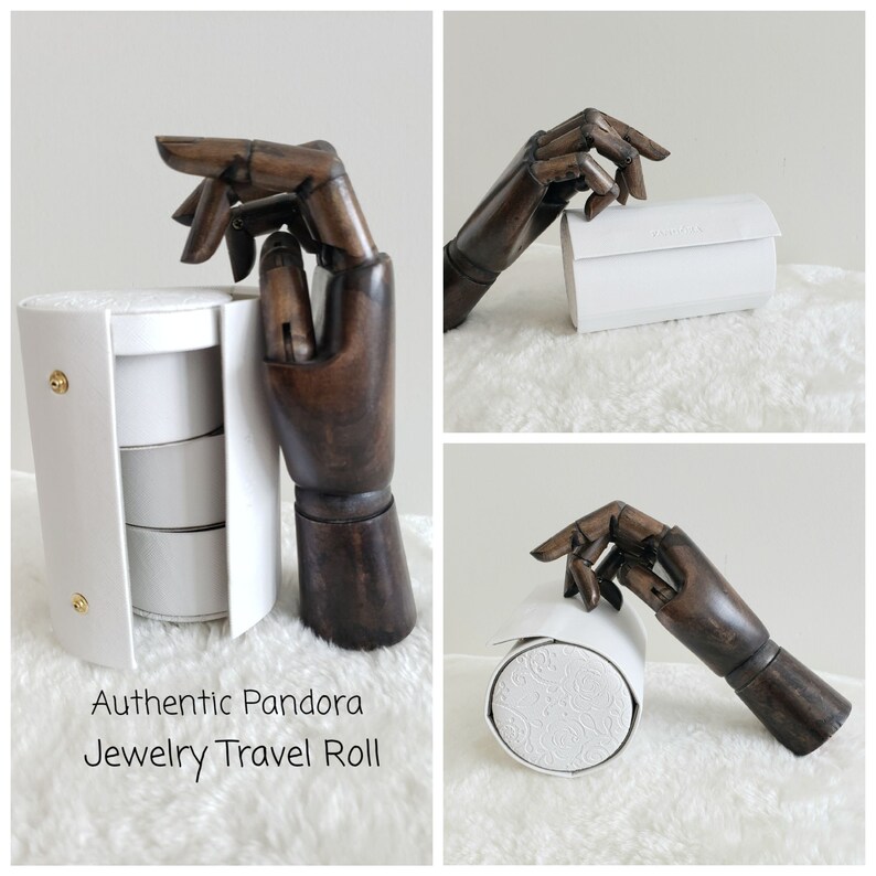 May include: White travel roll for jewelry with three compartments. The roll is made of faux leather and has a white embossed pattern. The roll is closed with a zipper. The text "Authentic Pandora Jewelry Travel Roll" is printed on the bottom of the image.