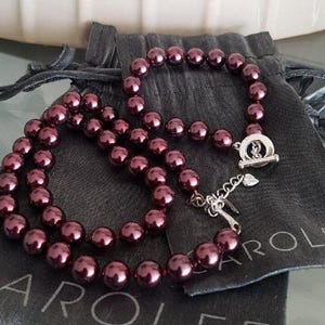 May include: A set of two burgundy pearl necklaces with silver clasps and a silver charm on a grey velvet pouch with the word "Carolee" printed on it.