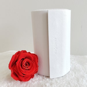 May include: A white cylindrical box with the word "Pandora" embossed on the side. The box is sitting on a white fluffy surface next to a single red rose.