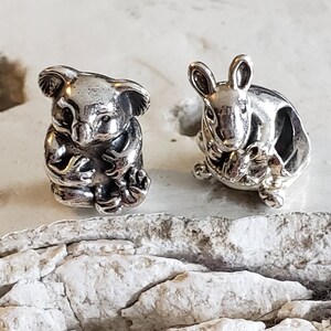May include: Two silver charm beads, one depicting a koala and the other a rabbit, both holding a smaller animal in their arms. The beads are detailed and have a realistic appearance.