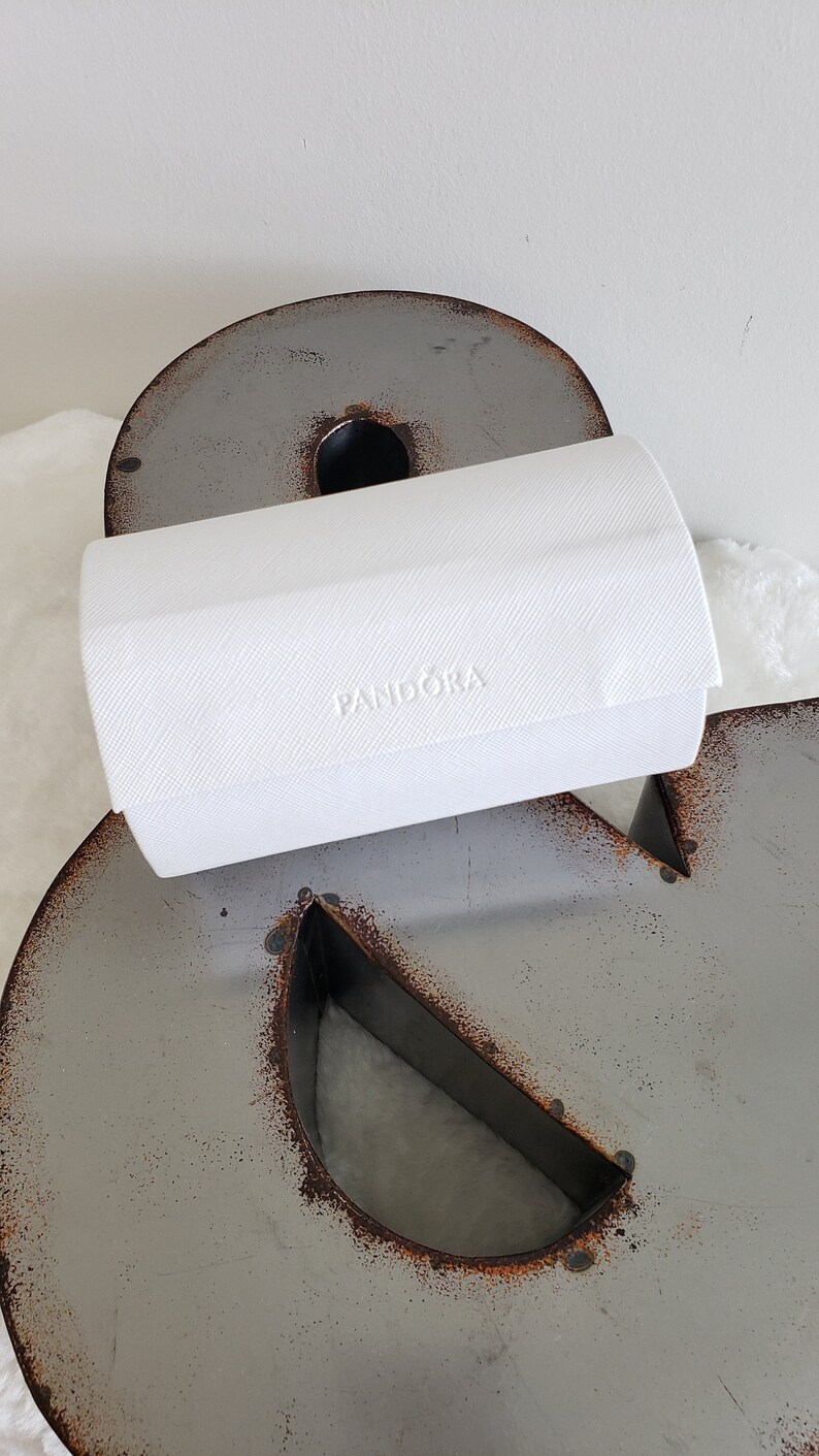 May include: A white rectangular box with the word "PANDORA" embossed on the top. The box is sitting on a gray metal surface.