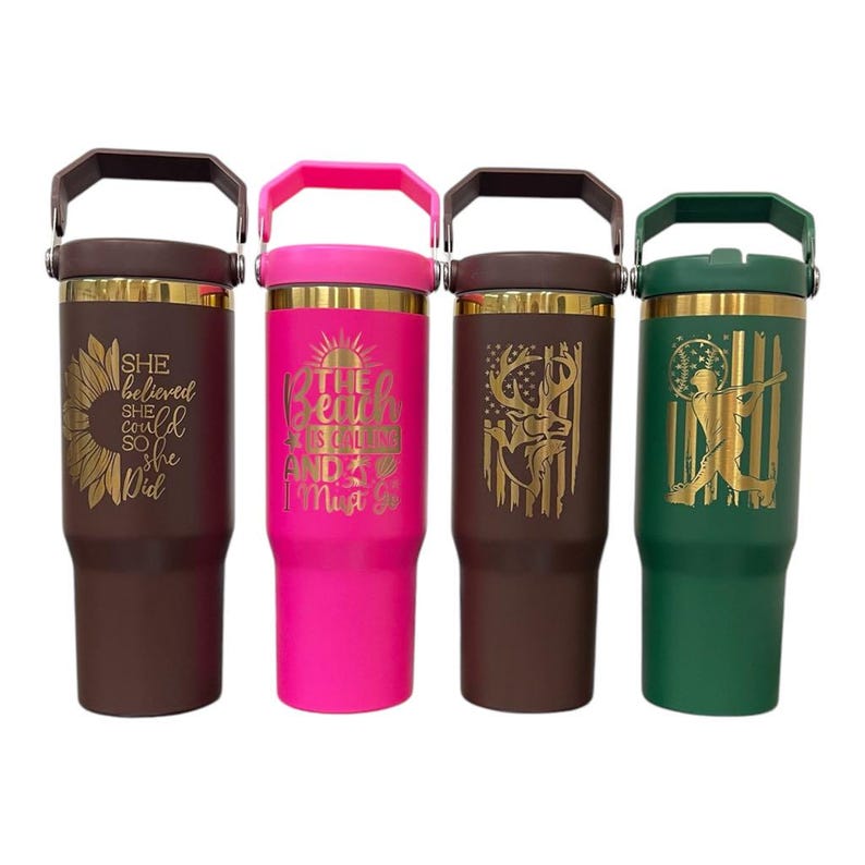 May include: Four insulated tumblers with handles. One is brown with a sunflower design and the text "She believed she could so she did." Another is pink with the text "The beach is calling and I must go." The third is brown with a deer and American flag design. The last is green with a baseball player design.