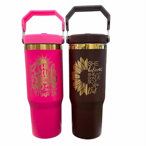 May include: Two insulated tumblers with handles. One is bright pink with the text "The beach is calling and I must go." The other is brown with a sunflower design and the text "She believed she could so she did."