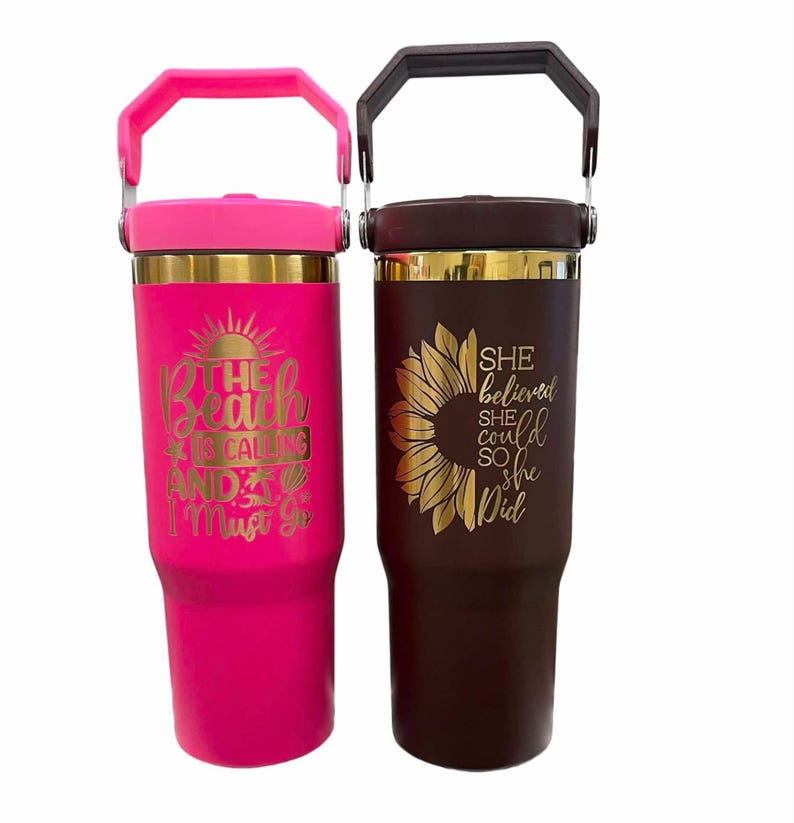 May include: Two insulated tumblers with handles. One is bright pink with the text "The beach is calling and I must go." The other is brown with a sunflower design and the text "She believed she could so she did."