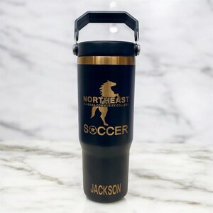 May include: A black insulated tumbler with a gold band and handle. The tumbler features the text "NORTHEAST ALABAMA COMMUNITY COLLEGE" and a gold horse graphic. Below the graphic is the word "SOCCER" and the name "JACKSON".