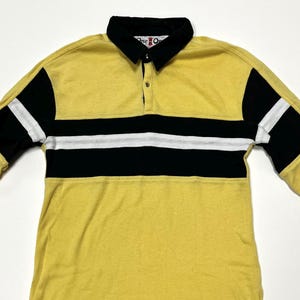 May include: Yellow long-sleeve shirt with black and white horizontal stripes across the chest. The shirt has a black collar and black accents on the sleeves. The shirt has a button-down collar and the text "One O" is visible on the collar.