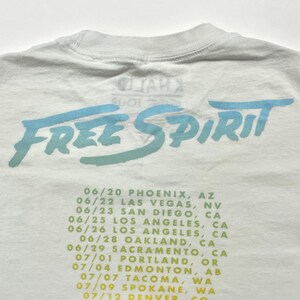 May include: White t-shirt with a blue and green "Free Spirit" graphic and a list of tour dates and locations printed on the back.