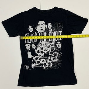 May include: Black t-shirt featuring a band graphic. The shirt displays the band name "Black Veil Brides" in white text above a collage of band members. The band's logo is also visible in white. The shirt is approximately 22 inches wide.