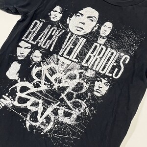 May include: Black t-shirt featuring a distressed white graphic of the band Black Veil Brides. The design includes the band's name and faces of the band members. The shirt is made of a soft, dark fabric.