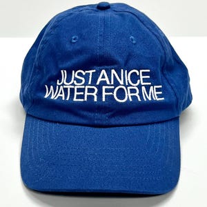 May include: A blue baseball cap with the text "JUST ANICE WATER FOR ME" embroidered in white. The cap has a curved brim and a button on top. The hat is made of a soft, durable fabric.