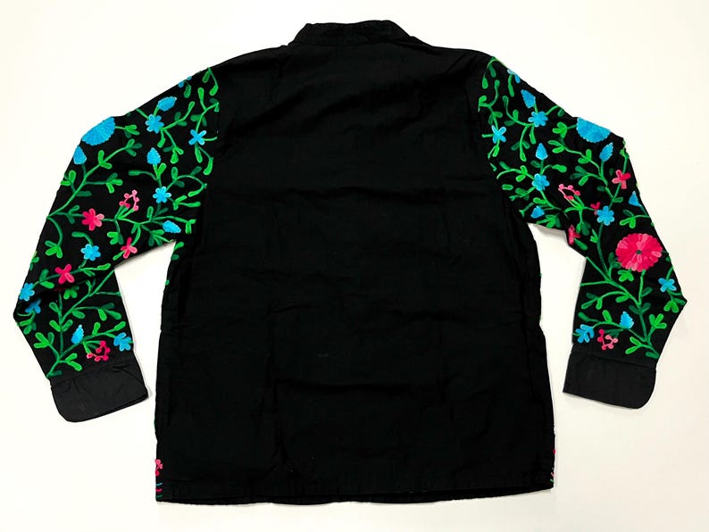 Op de afbeelding: Zwart shirt met lange mouwen en bloemenborduurwerk op de mouwen. Het borduurwerk heeft groene bladeren, roze en blauwe bloemen. Het shirt heeft een mandarijnkraag en manchetten met knopen. Het shirt is gemaakt van een zacht, comfortabel materiaal.