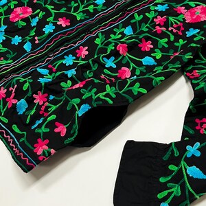 Op de afbeelding: Zwart overhemd met gedetailleerde bloemenborduurwerk. Het borduurwerk toont roze, blauwe en groene bloemen en ranken. Het overhemd heeft lange mouwen en een klassieke kraag. Het ontwerp is gedetailleerd en levendig.