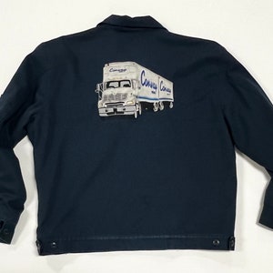 May include: A dark blue work jacket with a white semi-truck and trailer on the back. The truck has the word "Conway" printed on the side of the trailer.