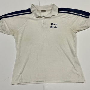 May include: White short-sleeved polo shirt with navy blue and white stripes on the sleeves. The shirt has a  "Penn State" logo embroidered on the front.