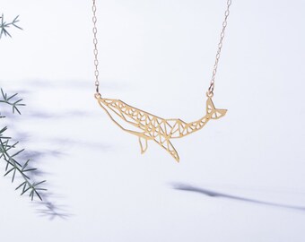 Op de afbeelding: Een goudkleurige ketting met een hanger in de vorm van een walvis. De walvishanger is opgebouwd uit een reeks onderling verbonden geometrische lijnen en driehoeken, wat een hol, opengewerkt ontwerp creëert dat aan een fijne metalen ketting hangt.