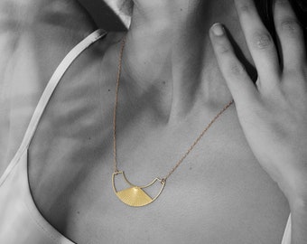 May include: A gold necklace with a geometric pendant shaped like a crescent moon with a sunburst design.