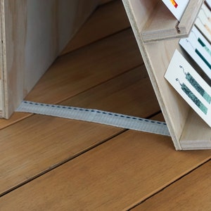 May include: A wooden display stand with multiple shelves, each holding a card with a green and white design. The stand is made of light wood and has a white strap attached to the bottom.