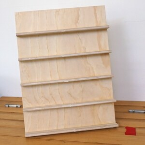 May include: A wooden shelf unit with five shelves. The shelves are made of plywood and are unfinished.