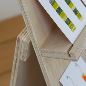 May include: A wooden display stand with multiple shelves for showcasing cards or other small items. The stand is made of light-colored wood with a natural finish.