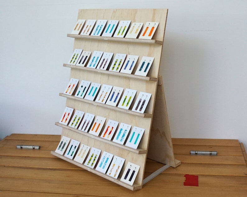 May include: A wooden display stand with five shelves holding colorful rectangular cards with pairs of earrings on each card.