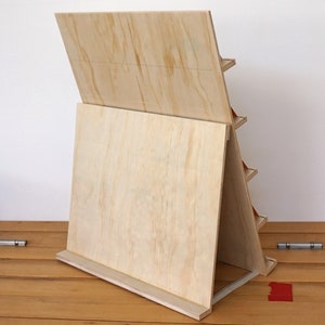 May include: A wooden display stand with multiple shelves, made of plywood with a natural wood finish. The stand is angled and has a back panel that can be used for displaying items.