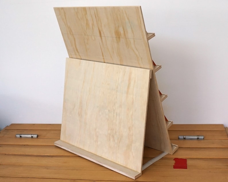 May include: A wooden display stand with multiple shelves, made of plywood with a natural wood finish. The stand is angled and has a back panel that can be used for displaying items.