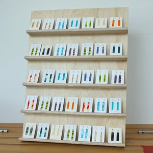 May include: A wooden display stand with five shelves holding a variety of colorful fabric earrings. The earrings are arranged in rows on small white cards.