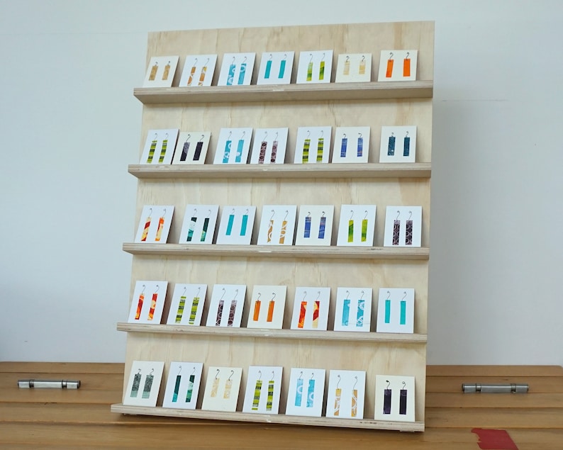 May include: A wooden display stand with five shelves holding a variety of colorful fabric earrings. The earrings are arranged in rows on small white cards.