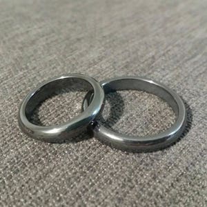 May include: Two simple silver rings, one slightly larger than the other, are interlocked and lying on a gray textured surface.