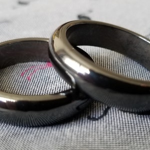 May include: Two black, polished, metal rings, stacked on top of each other. The rings are smooth and have a shiny finish.