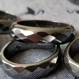 May include: Three black and silver rings with a faceted design. The rings are stacked on top of each other and are lying on a gray fabric surface.