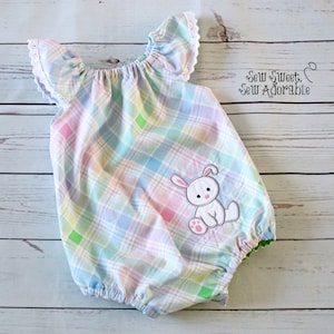 May include: A baby onesie with a pastel plaid pattern and a white bunny applique. The onesie has ruffled sleeves with white lace trim. The text "Sew Sweet, Sew Adorable" is visible in the upper right corner of the image.