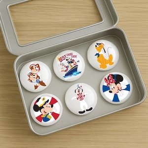May include: A set of six round, white magnets featuring Disney characters in a silver tin. The magnets showcase Mickey Mouse, Minnie Mouse, Pluto, Goofy, and Chip and Dale. One magnet reads "BEST CRUISE EVER!"