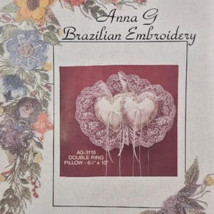 May include: A white double ring pillow with lace trim and two white hearts. The pillow is 6 1/2 inches by 10 inches. The text "AG-3110 DOUBLE RING PILLOW - 6 1/2" x 10" is printed below the pillow.