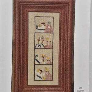 Può includere: Un ricamo a punto croce incorniciato che presenta una serie di scene con galline e maiali. La cornice è in legno marrone con una bordura dorata. Il testo "Bacon N eggs" è in alto nell'immagine e "Say Cheese" in basso.