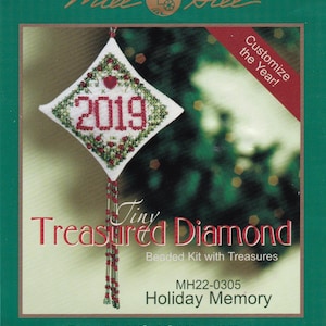 Può includere: Un ornamento bianco a forma di diamante con un cuore rosso e l'anno 2019 ricamato su di esso. L'ornamento è perlato e ha uno sfondo verde. Il testo "Tiny Treasured Diamond Beaded Kit with Treasures" è stampato sulla confezione. Il numero di prodotto MH22-0305 e il titolo "Holiday Memory" sono anche stampati sulla confezione. La dimensione finita è di 8,26 cm per 13,97 cm.