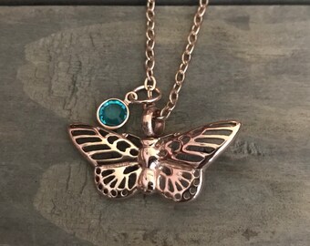 May include: A rose gold butterfly necklace with a teal blue crystal charm.