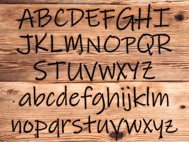 May include: A close-up of a wooden surface with the alphabet written in black marker. The letters are written in a casual, handwritten style. The letters are arranged in three rows, with the uppercase letters on the top row, the lowercase letters on the second row, and the lowercase letters on the third row.