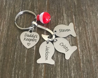 May include: Silver keychain with a red and white bobber, a heart charm that says "Daddy's Keepers", and three fish charms with the names "Jackson", "Christy", and "Steven" engraved on them.