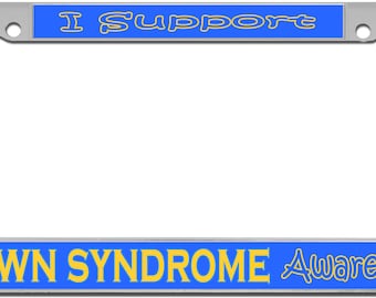May include: A silver license plate frame with a blue and yellow design. The top of the frame says "I Support" and the bottom says "Down Syndrome Awareness".