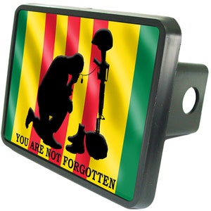 May include: A black hitch cover with a yellow, red, and green flag and a silhouette of a soldier kneeling with a rifle. The text "YOU ARE NOT FORGOTTEN" is printed on the cover.