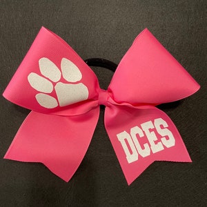May include: Pink cheer bow with a white paw print and the text "DCES" in white.