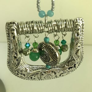 May include: A silver belt buckle with a decorative design and a chain with turquoise and green beads hanging from it.