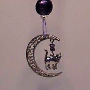 May include: Purple and silver beaded car charm with a crescent moon and a black cat hanging from it.