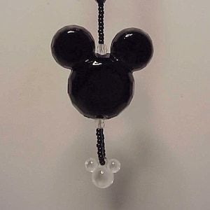 May include: Black and clear beaded car charm featuring a Mickey Mouse head with large black ears and a smaller clear bead set for the nose. The charm is attached to a black beaded string with a clear star bead.