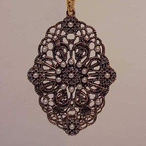 May include: A gold and silver filigree pendant with a floral design and pearl accents.