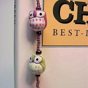 May include: A purple, green, and pink owl bead bookmark with a brown and black beaded chain.
