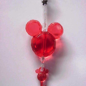 May include: Red crystal Mickey Mouse charm with a red crystal key charm hanging from it. The charms are attached to a clear beaded chain.
